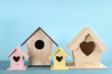 Photo of Beautiful bird houses on wooden table against light blue background