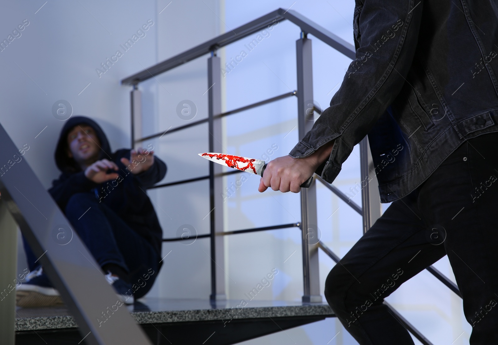 Photo of Criminal with knife attacking man on stairs indoors, closeup