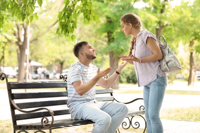 Photo of Young couple arguing while sitting on bench in park. Problems in relationship