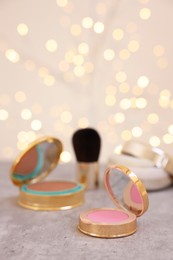 Photo of Face blusher and other cosmetic products on grey textured table against blurred lights, closeup. Space for text