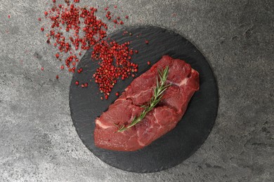 Photo of Piece of raw beef meat, rosemary and red peppercorns on grey table, flat lay