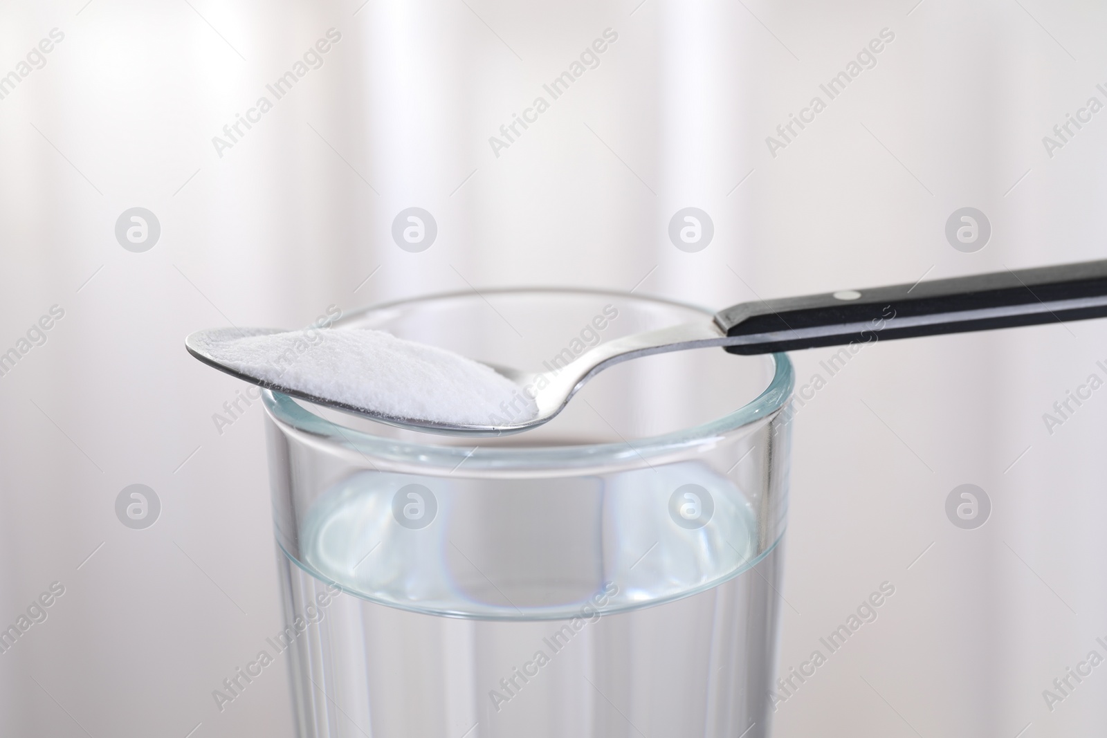 Photo of Glass of water and spoon with baking soda on light background, closeup