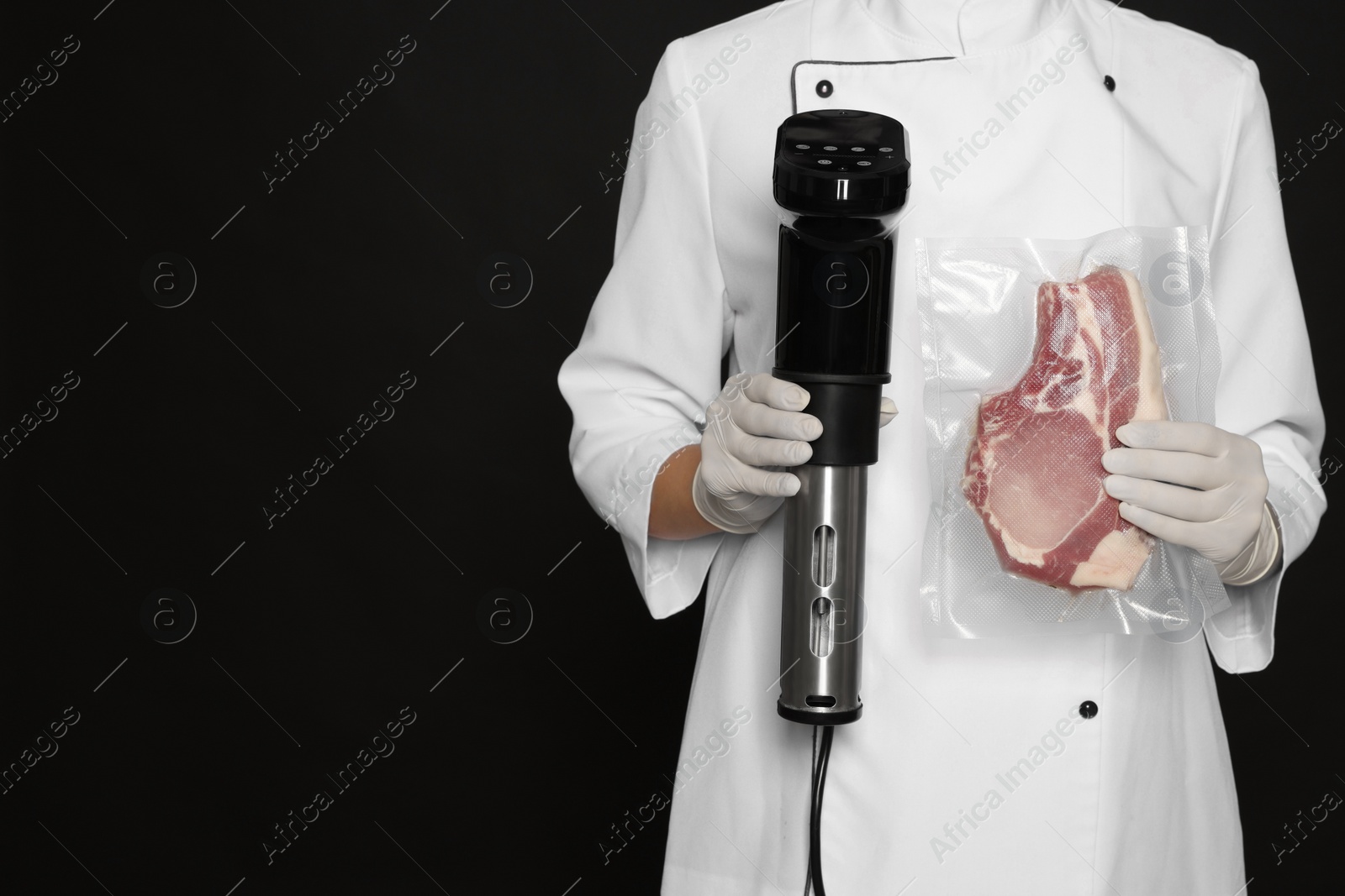 Photo of Chef holding sous vide cooker and meat in vacuum pack on black background, closeup. Space for text