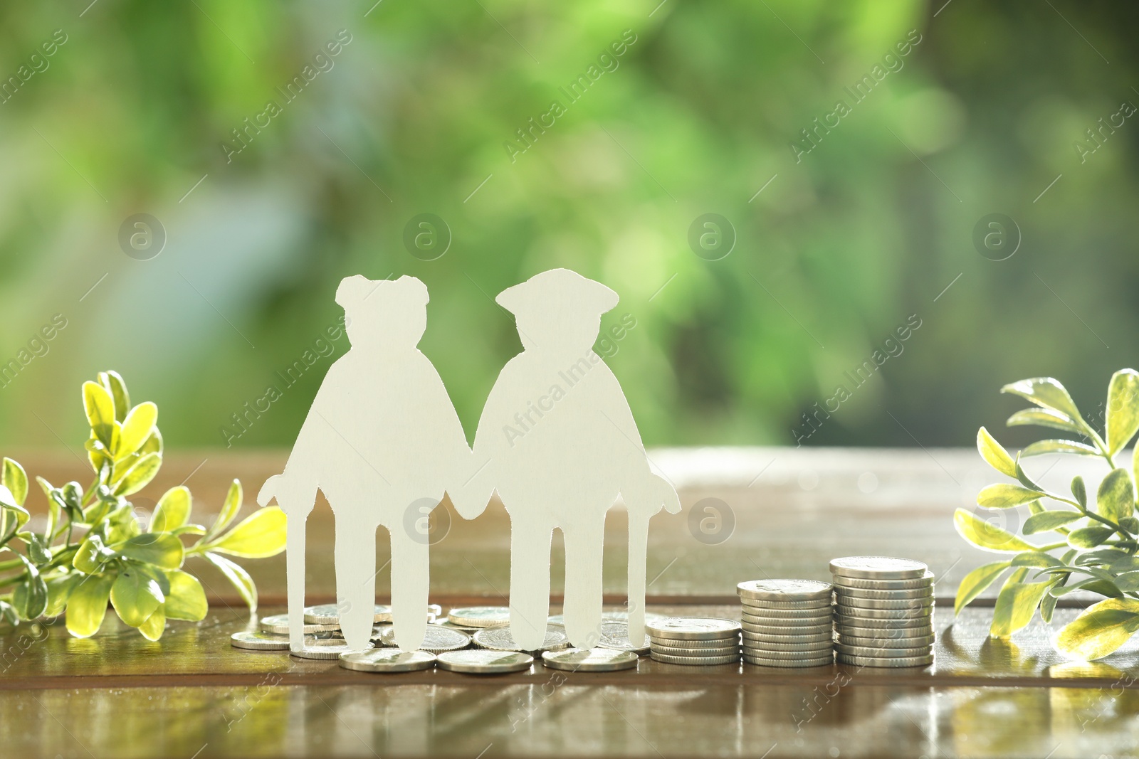 Photo of Pension savings. Figure of senior couple, coins and green twigs on wooden table outdoors