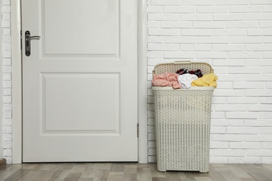 Photo of Plastic laundry basket full of dirty clothes near brick wall in room. Space for text