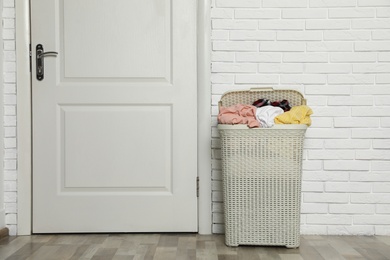 Plastic laundry basket full of dirty clothes near brick wall in room. Space for text