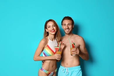 Happy young couple in beachwear with cocktails on color background