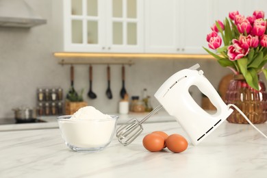 Photo of Modern mixer, eggs and bowl with flour on white marble table in kitchen