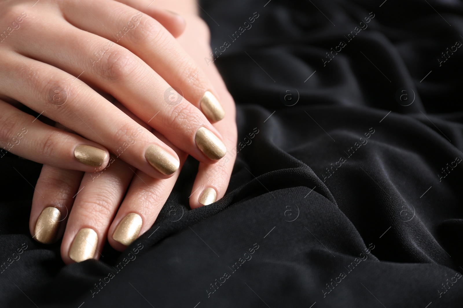 Photo of Woman showing gold manicure on black fabric, closeup with space for text. Nail polish trends