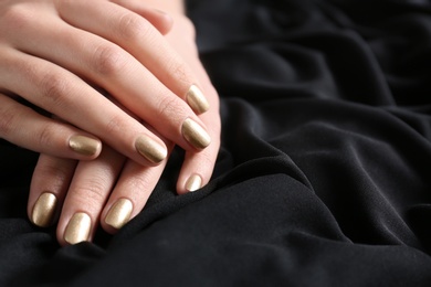 Photo of Woman showing gold manicure on black fabric, closeup with space for text. Nail polish trends