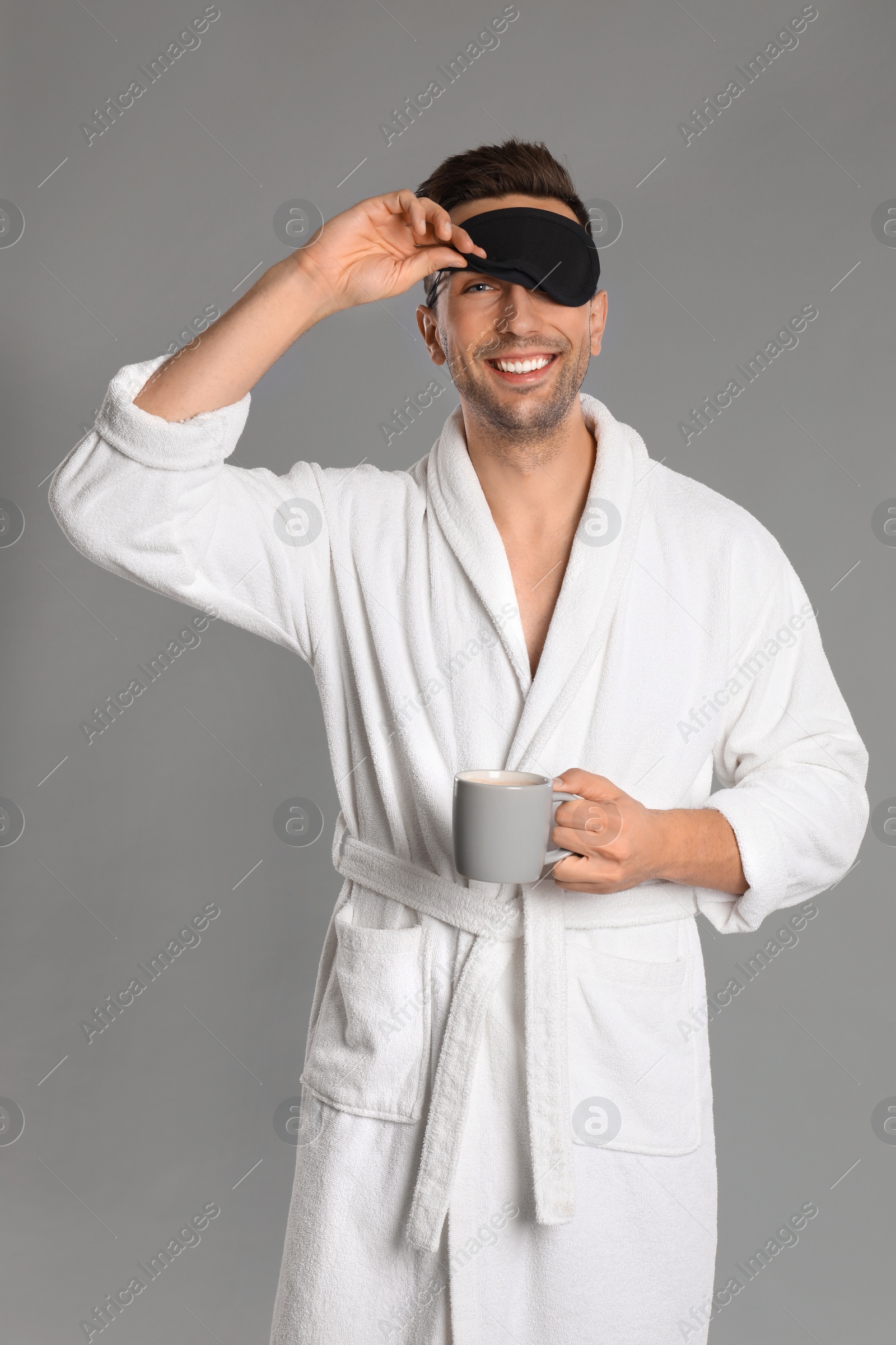 Photo of Happy young man in bathrobe with cup of coffee on grey background