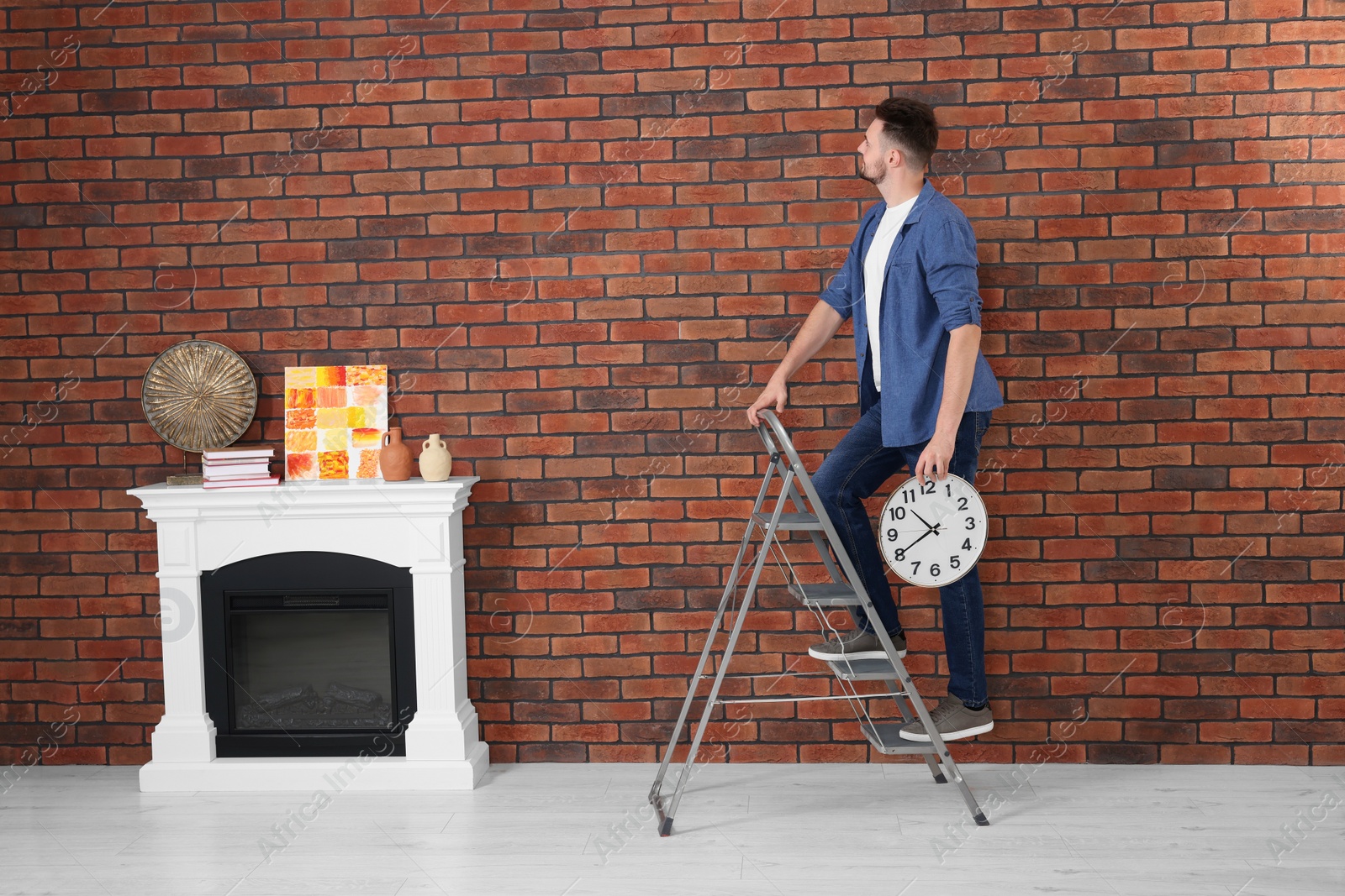 Photo of Man on stepladder hanging clock at home