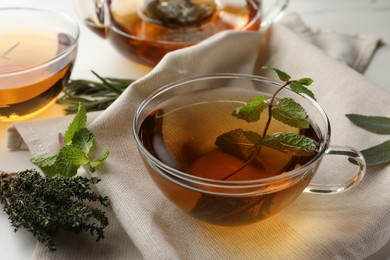 Cup of aromatic herbal tea with rosemary, sage, thyme and mint on table