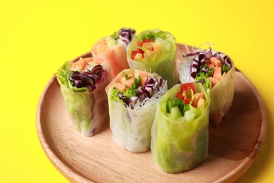 Different delicious spring rolls wrapped in rice paper on yellow background, closeup