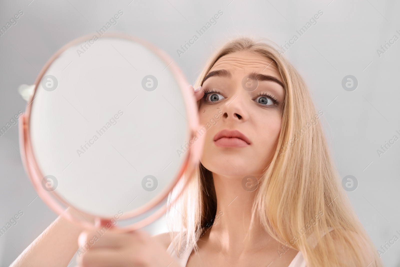 Photo of Young woman with eyelash loss problem looking in mirror indoors