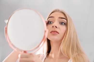 Young woman with eyelash loss problem looking in mirror indoors