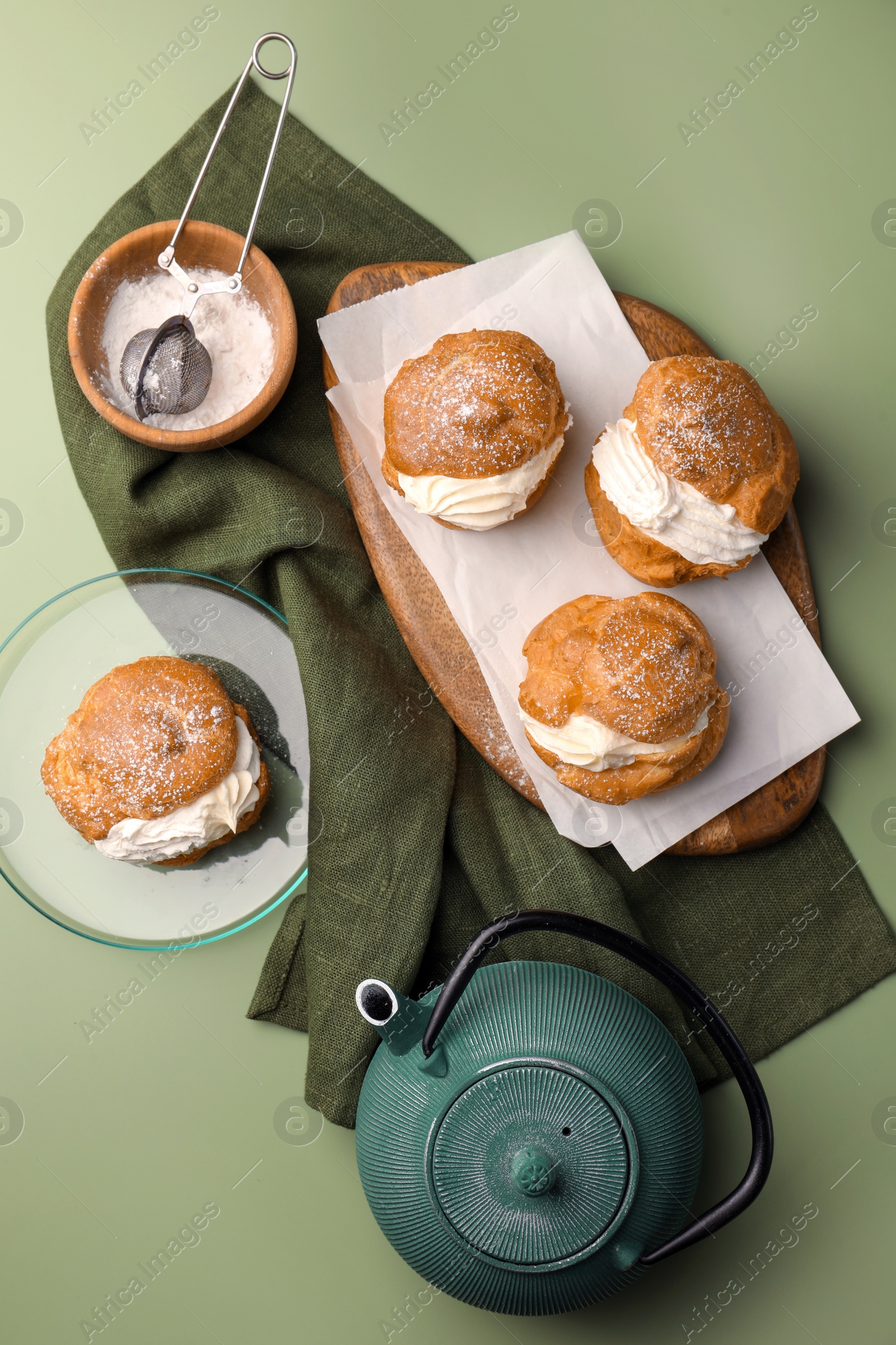 Photo of Delicious profiteroles filled with cream and teapot on green background, flat lay