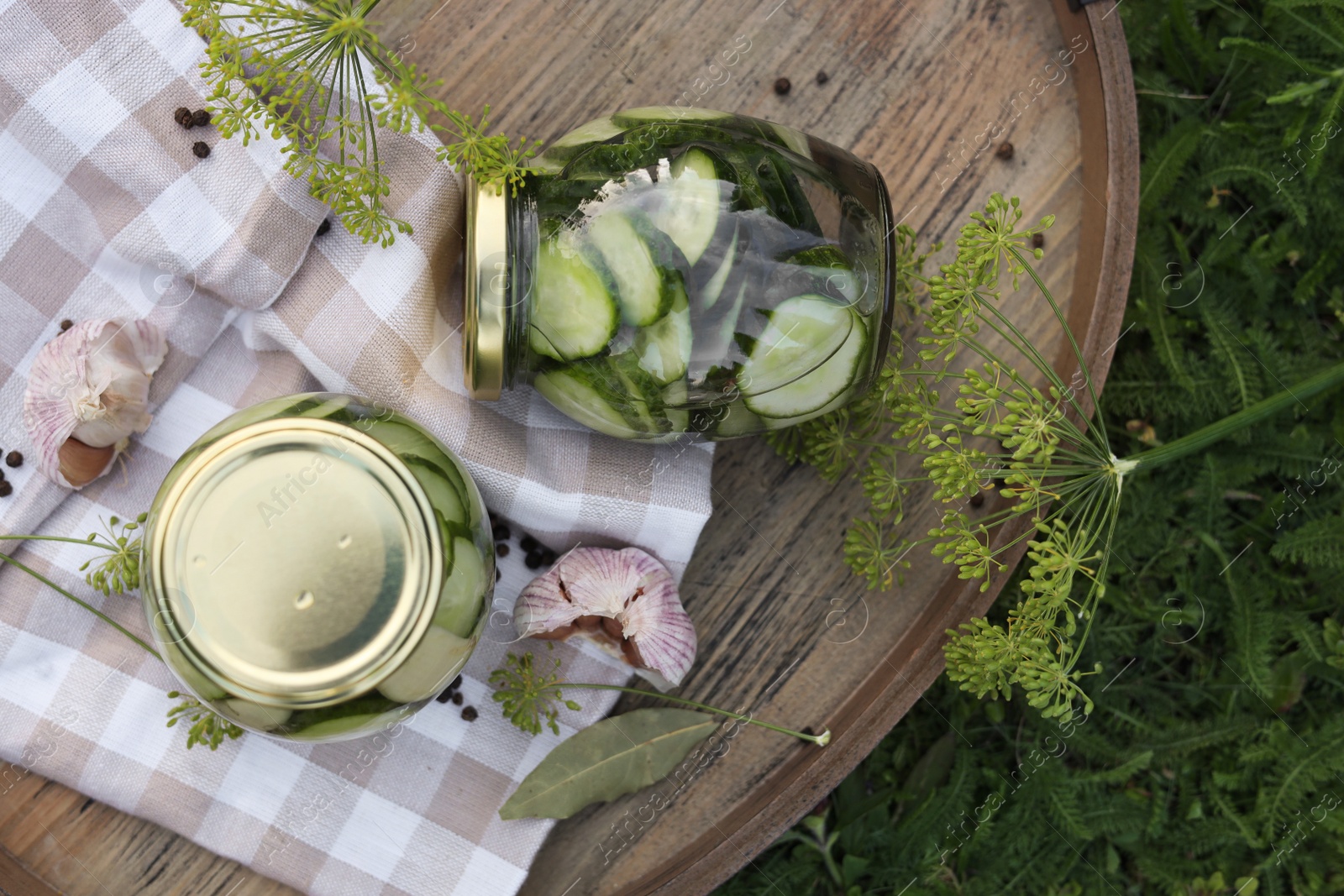 Photo of Jar of delicious pickled cucumbers on wooden tray outdoors, flat lay