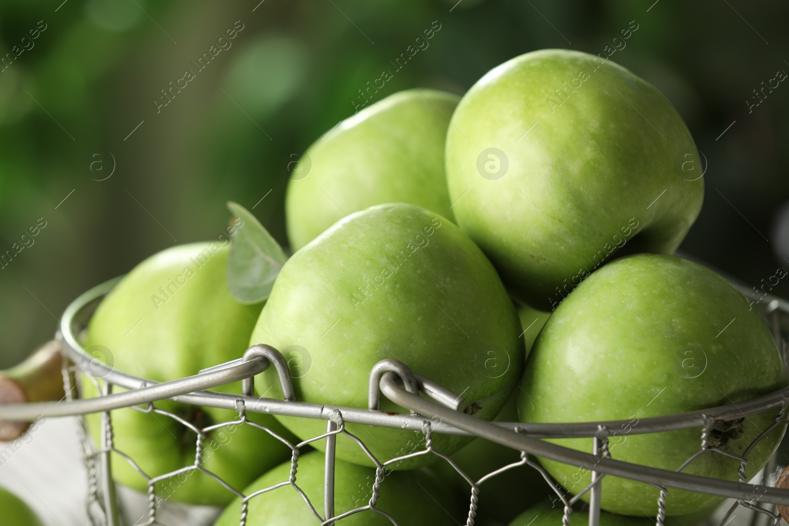 Photo of Metal basket with ripe green apples on blurred background, closeup