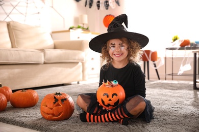Photo of Cute little girl with pumpkin candy bucket wearing Halloween costume at home