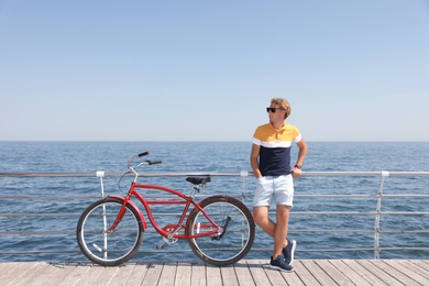 Attractive man with bike near sea on sunny day