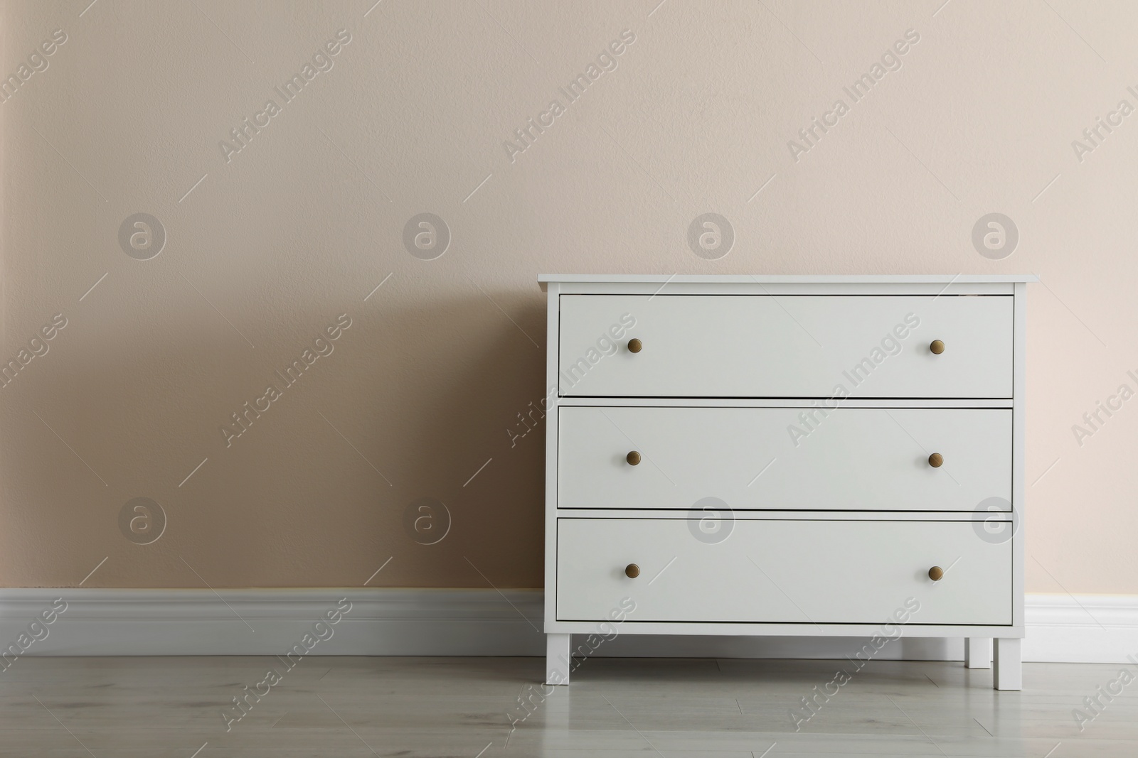 Photo of White chest of drawers near beige wall. Space for text