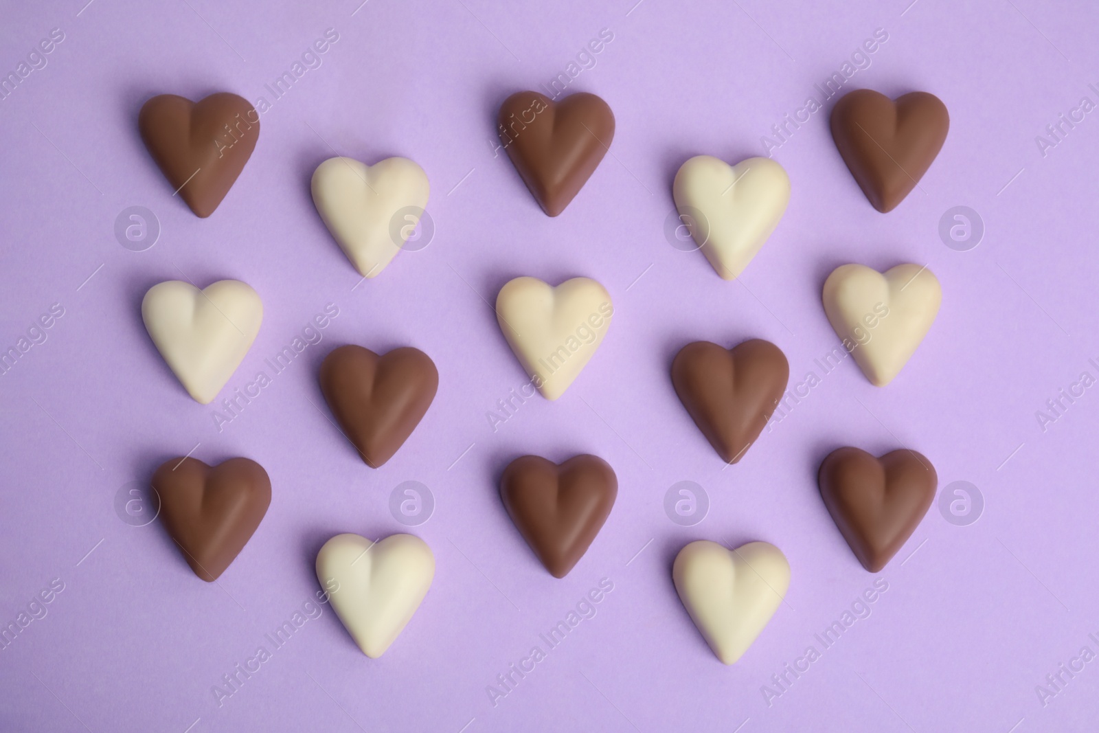 Photo of Tasty heart shaped chocolate candies on violet background, flat lay. Happy Valentine's day