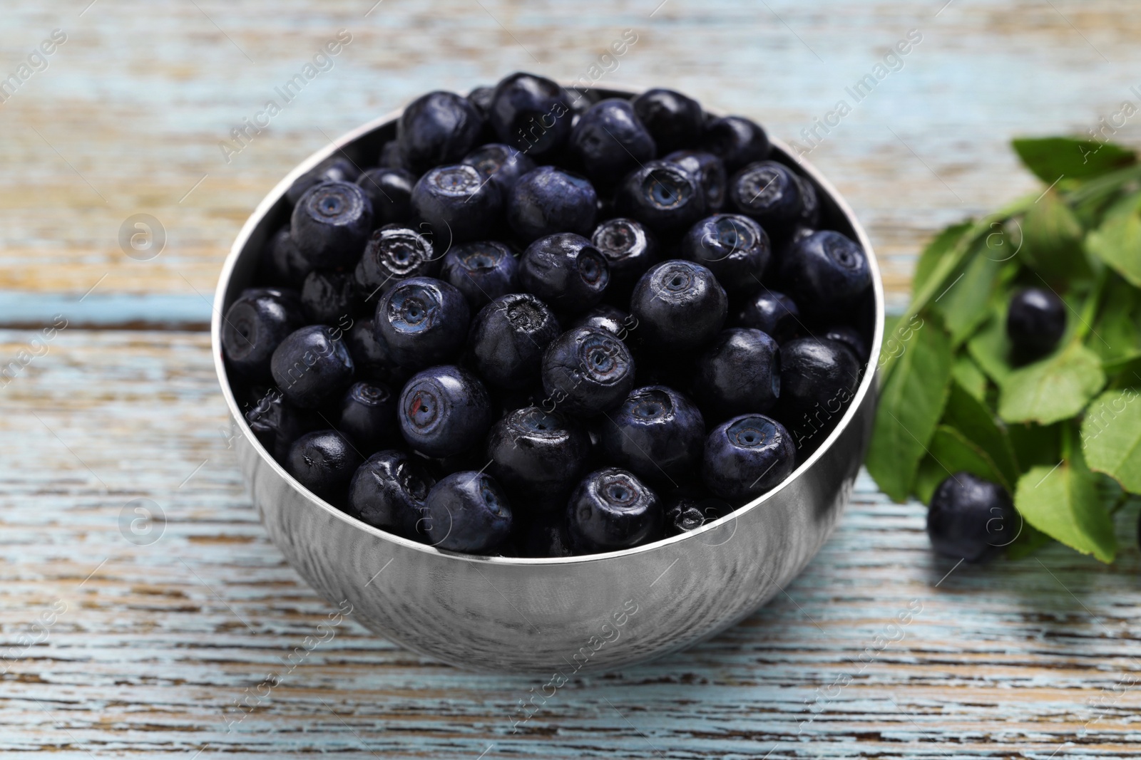 Photo of Ripe bilberries in bowl and leaves on wooden rustic table, closeup