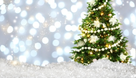 Image of Snow and beautiful decorated Christmas tree against blurred festive lights, bokeh effect. Space for text