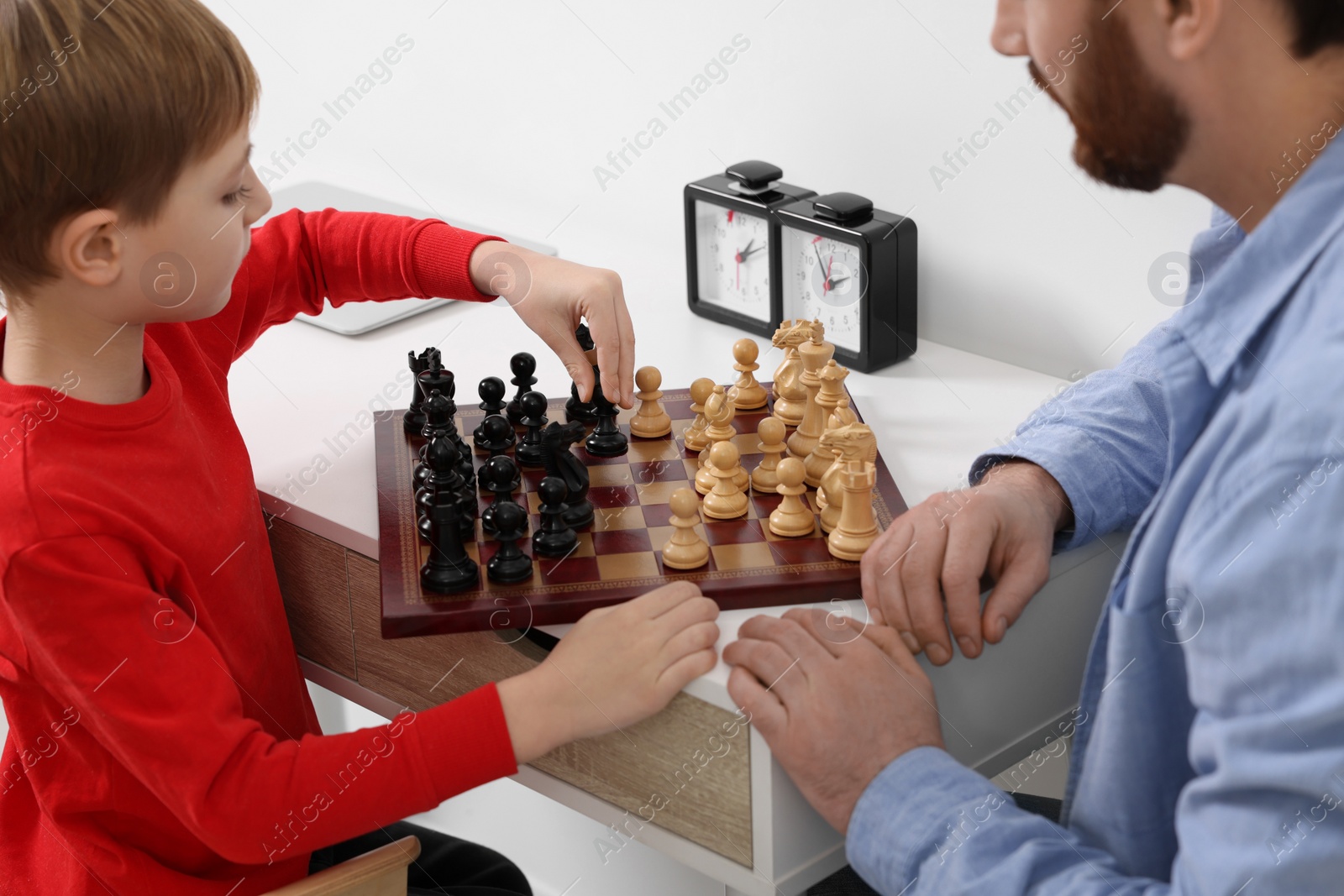 Photo of Father and son playing chess at table indoors, closeup