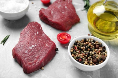 Fresh raw meat steaks and spices on light grey table, closeup