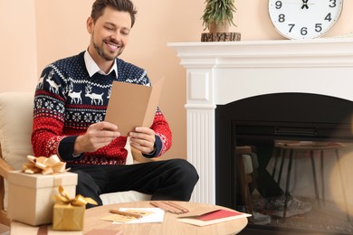 Photo of Happy man reading Christmas greeting card in living room
