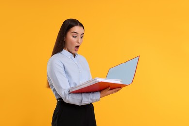 Photo of Shocked woman with folder on orange background