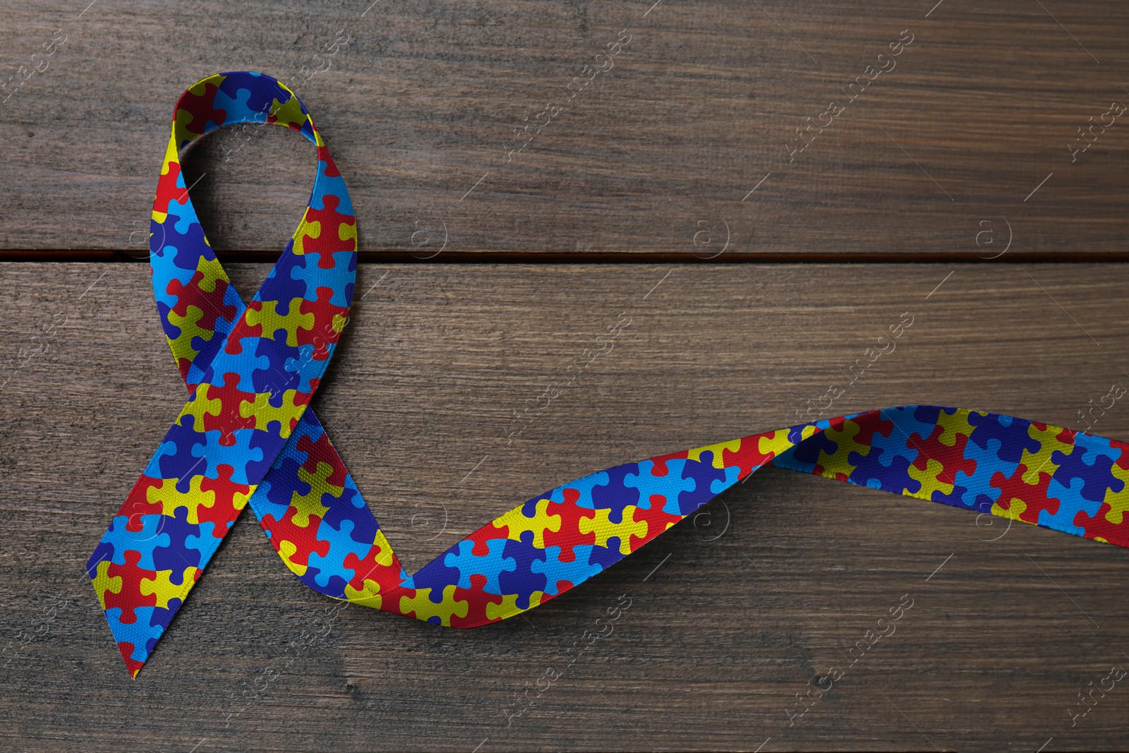 Image of World Autism Awareness Day. Colorful puzzle ribbon on wooden background, top view