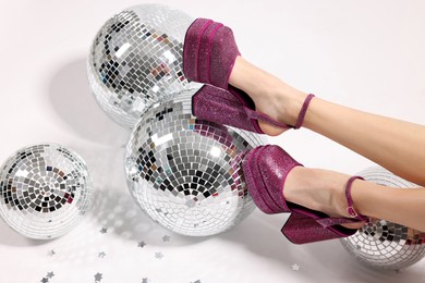 Photo of Woman in pink high heeled shoes and disco balls on white background, closeup
