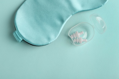 Photo of Pair of ear plugs in case and sleeping mask on turquoise background, flat lay