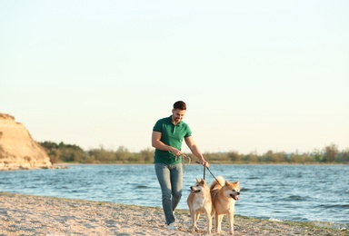 Photo of Young man walking his adorable Akita Inu dogs near river