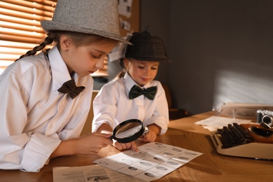 Cute little detectives exploring fingerprints with magnifying glasses at table in office