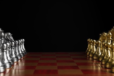 Many chess pieces on wooden checkerboard against black background, closeup. Space for text