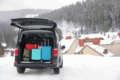 Photo of Black car with luggage in trunk on snowy road. Winter vacation