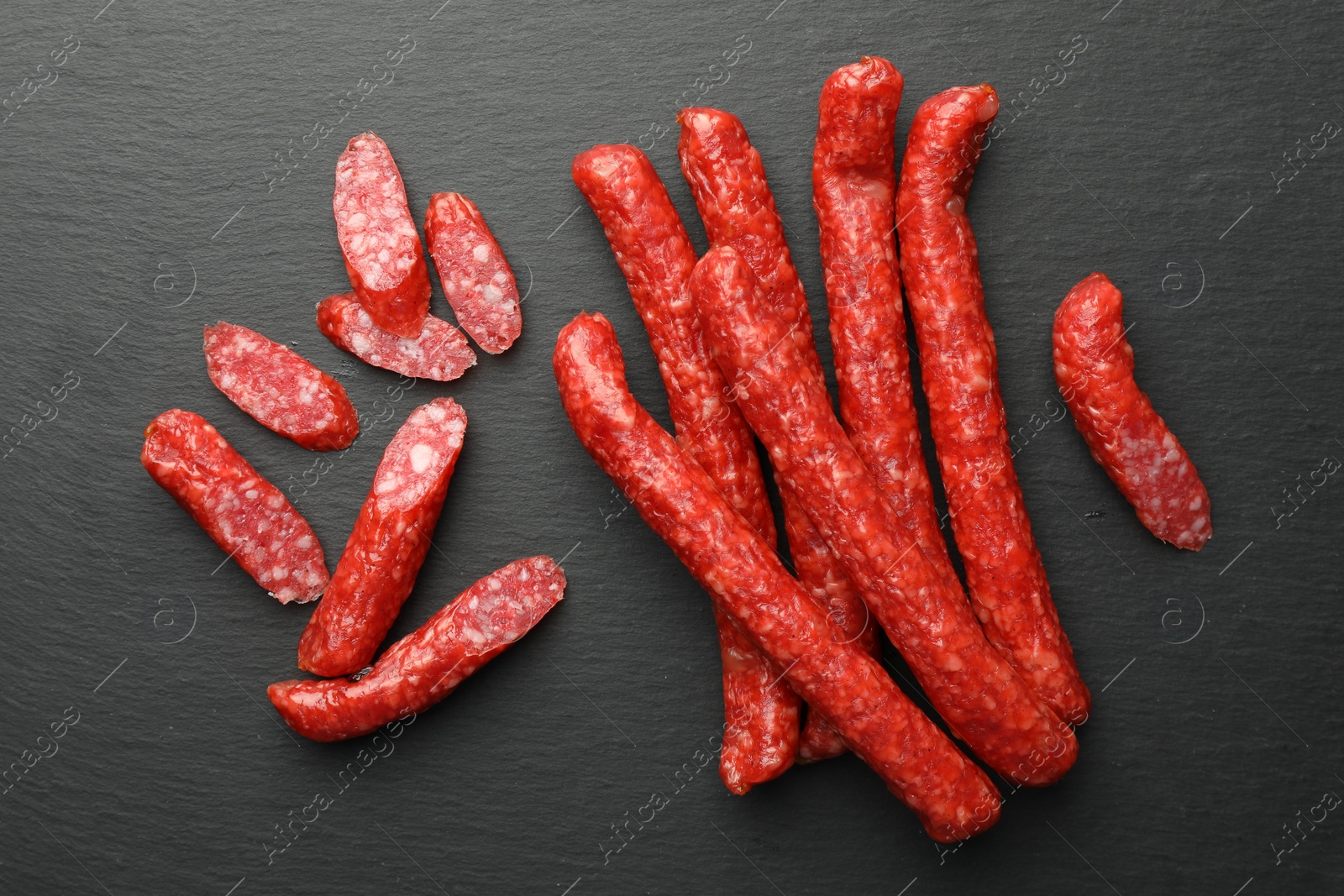 Photo of Many thin dry smoked sausages on black table, flat lay