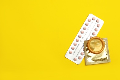 Condoms and birth control pills on yellow background, flat lay with space for text. Safe sex concept