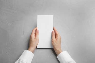 Photo of Young woman holding blank brochure at grey table, top view. Mock up for design