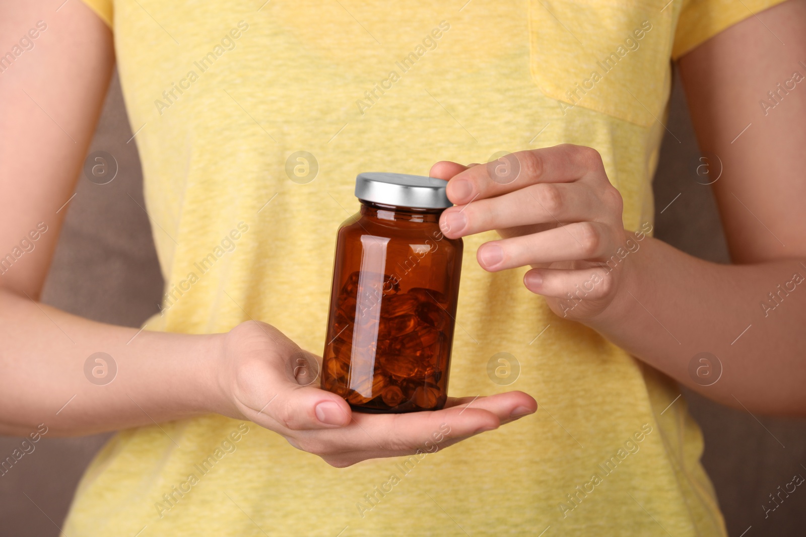 Photo of Woman holding bottle with vitamin capsules against light brown background, closeup