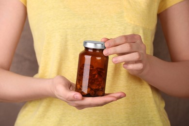 Woman holding bottle with vitamin capsules against light brown background, closeup