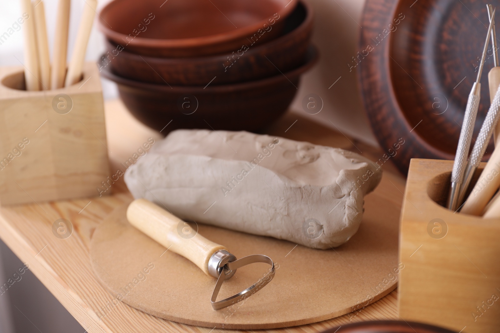 Photo of Set of different crafting tools and clay dishes on wooden table in workshop, closeup