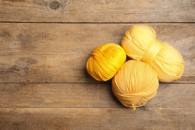 Soft yellow woolen yarns on wooden table, flat lay. Space for text