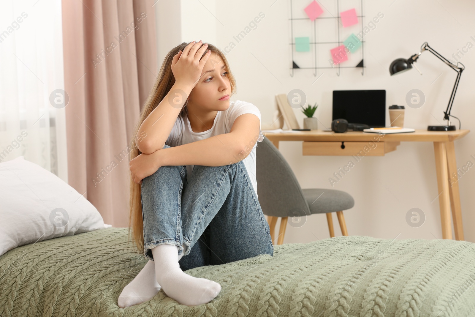 Photo of Upset teenage girl sitting on bed at home