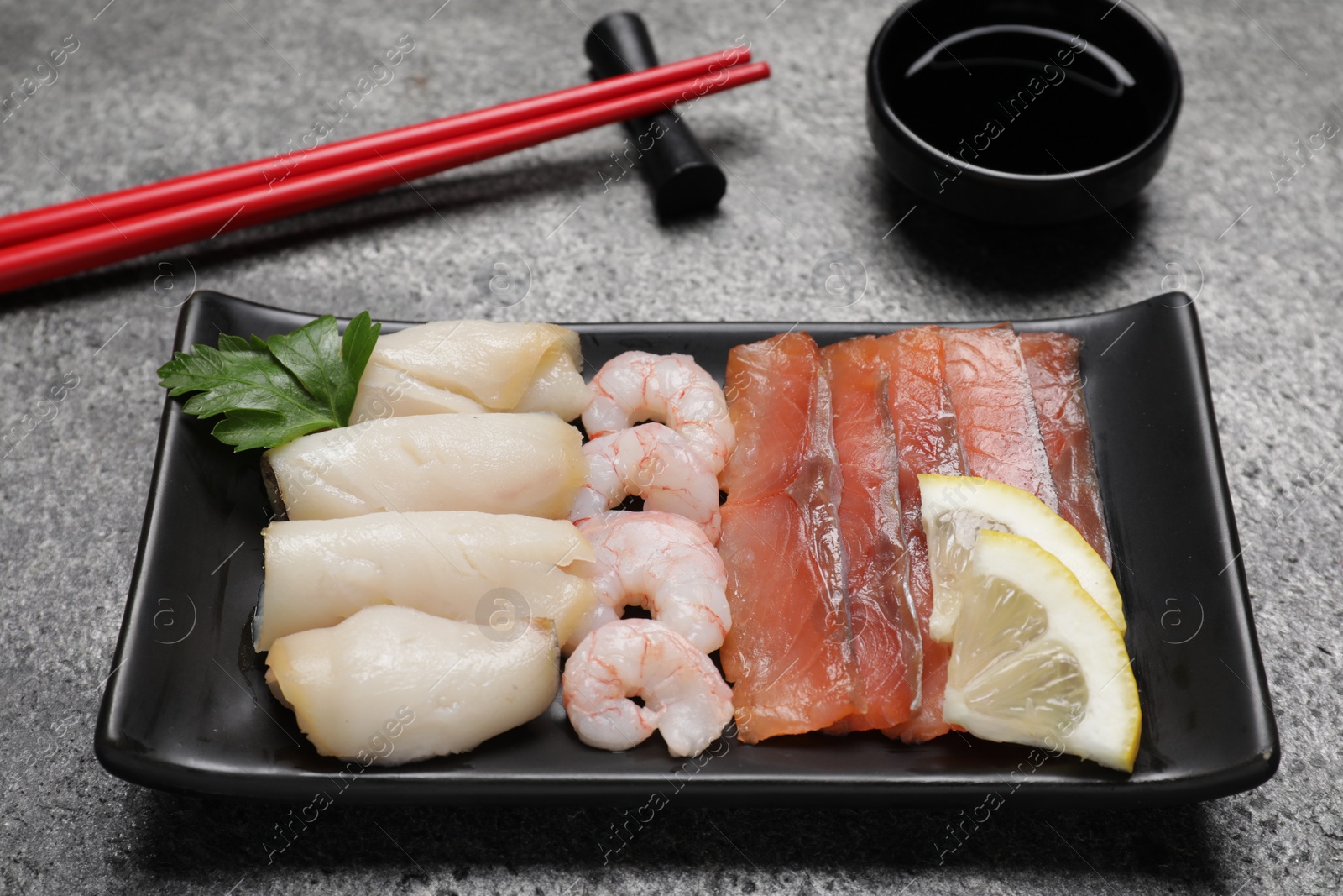 Photo of Sashimi set served with soy sauce, lemon and parsley on light grey table