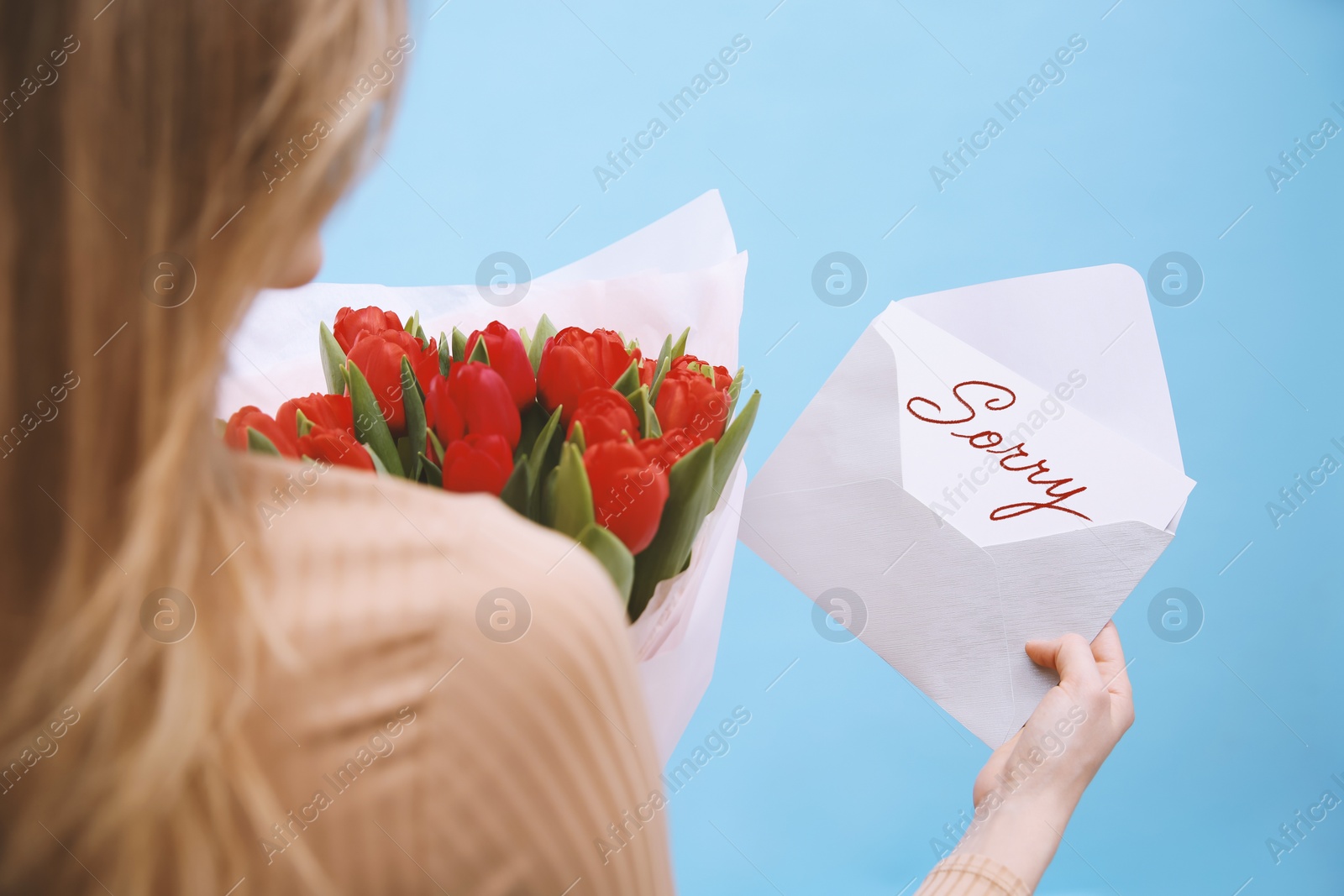 Image of Apology. Woman holding Sorry greeting card and bouquet of tulips on light blue background, closeup